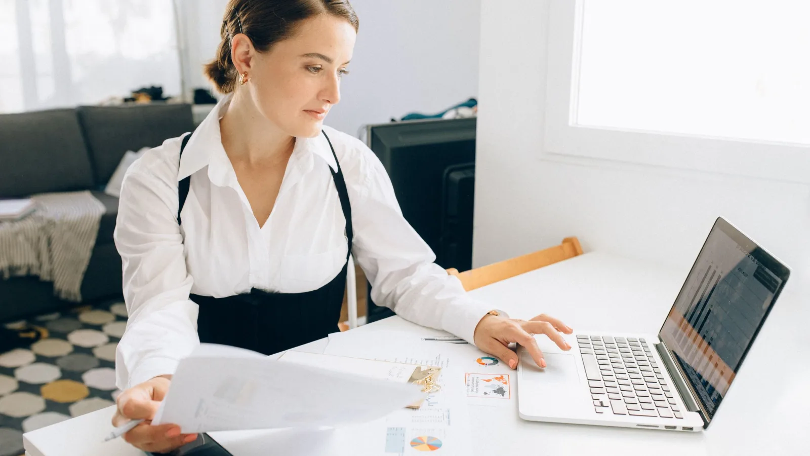 Person holding papers beside an open laptop