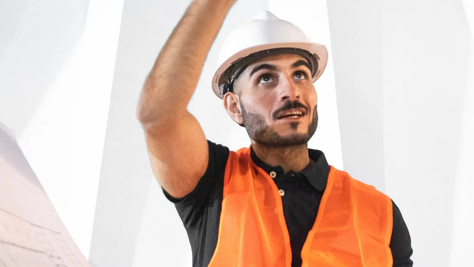Field worker in safety gear pointing above a partial paper plan